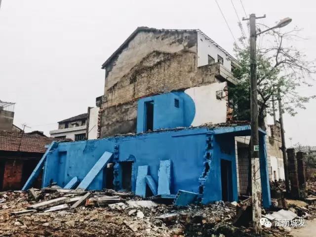 △ 這棟建筑是臨江最近的半拆遷建筑物的遺留，沅江和堤壩成為了展覽的天然背景。創(chuàng)作團(tuán)隊(duì)對(duì)這棟建筑進(jìn)行了半涂裝，將符號(hào)性的沅水曲線與拆遷進(jìn)行中的建筑立面進(jìn)行意義的疊造，它們共同觸發(fā)了場(chǎng)所空間多元語(yǔ)境的生成，把拆遷這種暫時(shí)破壞性、干擾性的介入行動(dòng)與沅水右岸發(fā)展的未來(lái)性、美好性緊密融合。